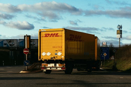 A DHL delivery truck driving on a highway intersection under a blue sky, displaying logistics in motion.